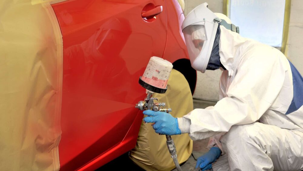 a person in a white suit painting a red car