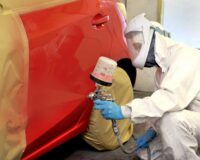 a person in a white suit painting a red car