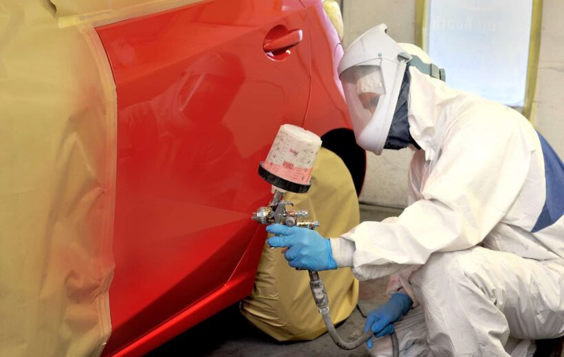 a person in a white suit painting a red car