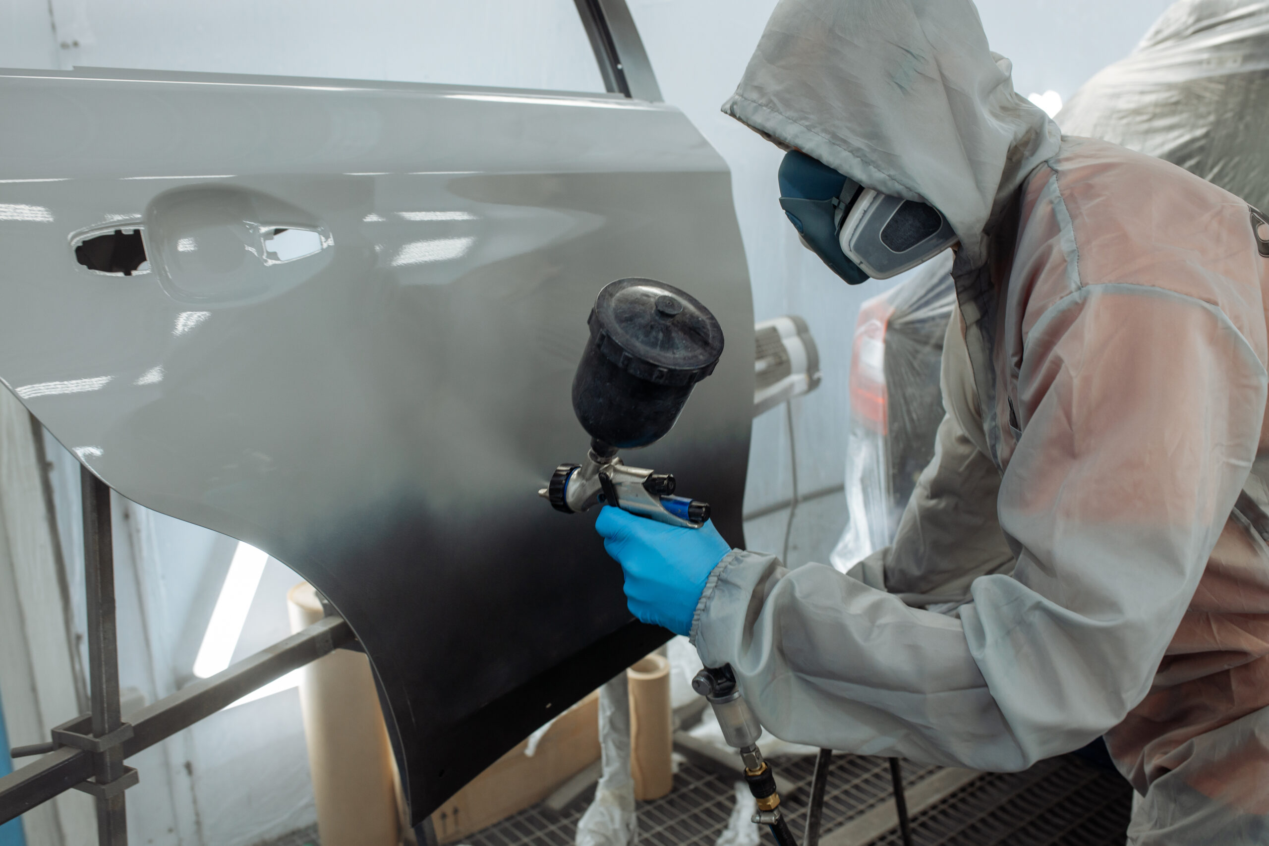 a person wearing a mask and gloves painting a car